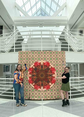 Zoom image: MFA Candidate Cristiano Pereira (MFA '24) and CFA House Manager Moriah Hegmann, posing by Pereira's works: &quot;Encruza&quot;, 2023, Oil on canvas with beads, 63&quot; diameter, and &quot;Goiaba&quot;, 2023, Archival Inkjet print on paper, variable dimensions. 