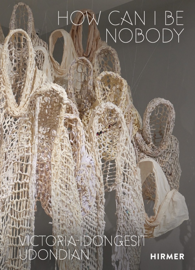Sculptures made out of crocheted rope, that look like life-sized hooded figures, with a gray background, and white text. 