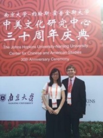 UB graduate Daniel Loebell posing in front of of the John Hopkins University-Nanjing University Center for Chinese and American Studies 10th Anniversary Ceremony poster. 