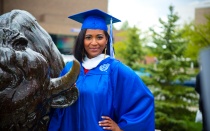 Student in graduation gown with Buffalo statue. 
