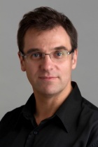 Prof. Jochen Autschbach wearing wire rimmed eyeglasses and a dark colored collared shirt. 