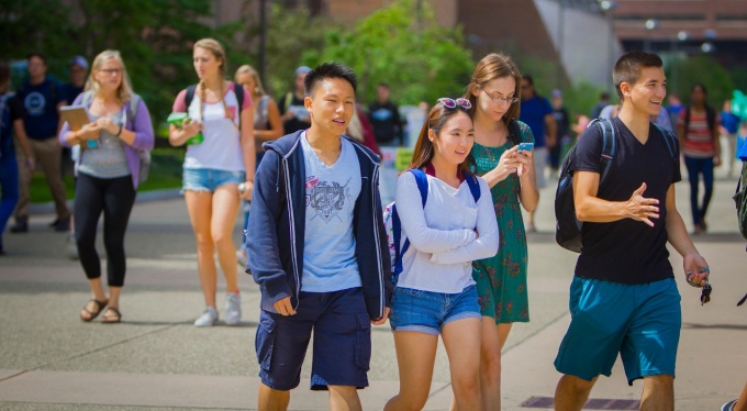 Pictured, busy students on UB’s campus move past the camera – talking, checking their phones, carrying books – on their way to classes. 