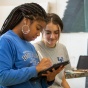 Two students look down at a rendering on a tablet in an art class. 