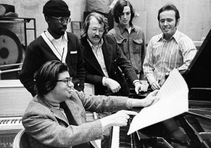 An archival photograph of Morton Feldman, seated at piano, surrounded by Creative Associates including composer David Del Tredici, percussionist Jan Williams and composers Julius Eastman and William Appleby. Photo: UB Libraries. 