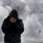 Man with hands covering his face, clouds of smoke behind him. 
