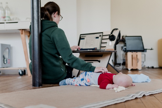A women working on her laptop and watching over a baby. 