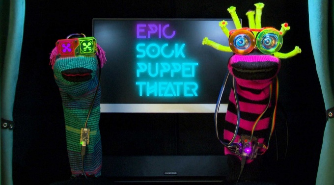 Screenshot of a a video from an art project, Epic Sock Puppet Theater, with two sock puppets, with lights for eyes. 