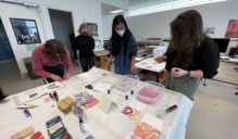 Kelly Myers-Chunco presents a marbled paper and block printing workshop. A table holds a number of trays filled with water and pigmented ink. Several students are working with the materials. 