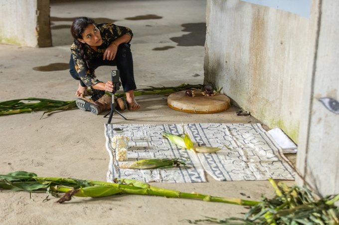 Jimena Murabito crouched and barefoot on a cement floor, working on a site-specific performance for Professor Millie Chen’s course, Installation: Urban Space, within a grain silo at "Silo City" in Buffalo, with cloth and ears of corn arranged on the ground in front of her. 