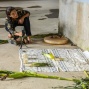 Jimena Murabito crouched and barefoot on a cement floor, working on a site-specific performance for Professor Millie Chen’s course, Installation: Urban Space, within a grain silo at "Silo City" in Buffalo, with cloth and ears of corn arranged on the ground in front of her. 