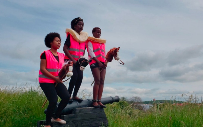 three people in pink safety vests on hobby horses. 