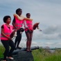 three people in pink safety vests on hobby horses. 