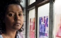 Crystal Z Campbell standing by window with colored fabrics. 