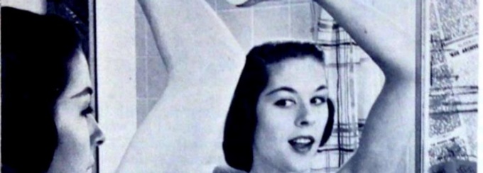 Woman with arm raised looking into a mirror, examining her underarm. 