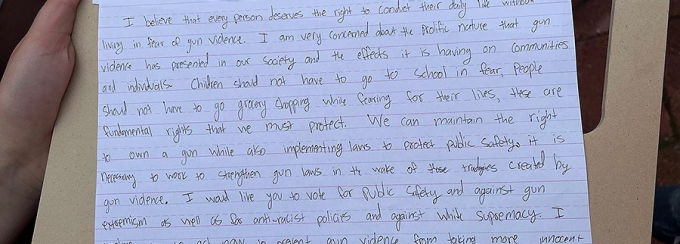 Handwritten letter on lined paper, resting on a clipboard held by hand. 