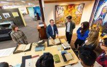 Art lecturer Kelly Myers-Chunco (far left) looks on while James Maynard (second from left), curator of the Poetry Collection and coordinator of the Rare & Special Books Collection, highlights one of the books he selected for students in Myers-Chunco&rsquo;s typography class to examine. Photo: Douglas Levere. 