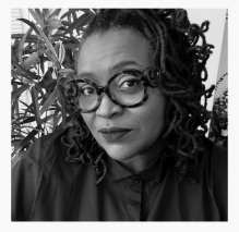Black and white headshot of artist Deborah Jack, wearing a button up shirt and large round, tortoise-patterned glasses. 