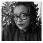 Black and white headshot of artist Deborah Jack, wearing a button up shirt and large round, tortoise-patterned glasses. 