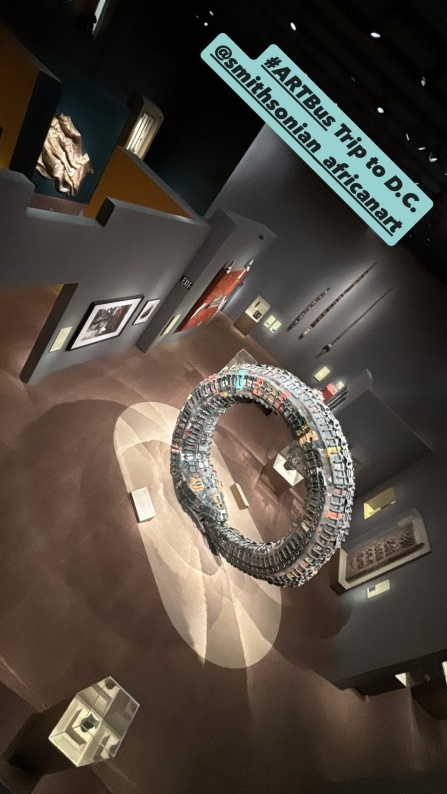 Large tire sculpture in the Museum of African Art in Washington D.C., as seen from a balcony above, and other artworks on the surrounding walls. 