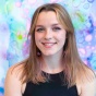 Headshot of Emma Stanton, wearing a black high-neck tank top, in front of a cool colors bubble pattern background. 