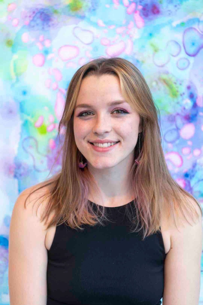 Headshot of Emma Stanton, wearing a black high-neck tank top, in front of a cool colors bubble pattern background.