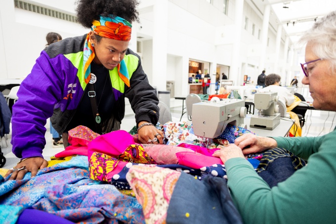 Zoom image: UB Art Alumnus Naija Boles, (2023 BFA), assisting Browder with the workshops, guides a community member with sewing panels for the collaborative tapestry. 