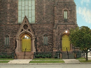 Romanesque redstone church front entrance, with two sets of yellow-ish green painted wood front doors. 