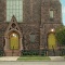 Romanesque redstone church front entrance, with two sets of yellow-ish green painted wood front doors. 