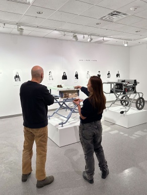 Two people stand in an art gallery with a replica tablesaw in the middle. 