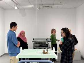 Five people stand in an art gallery with a replica tablesaw in the middle. 