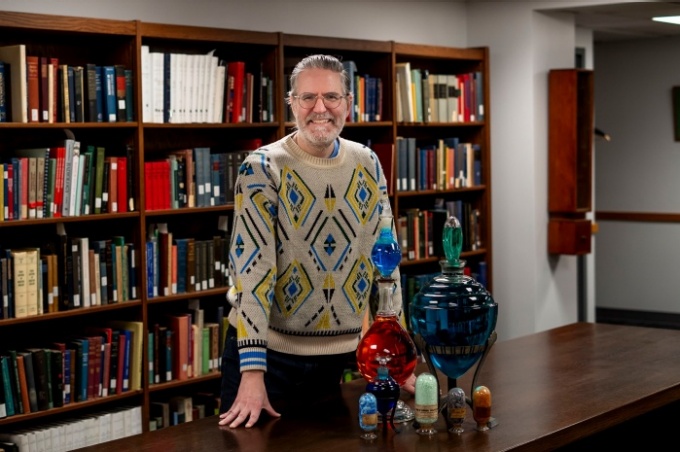 Zoom image: Keith Mages, curator of UB&rsquo;s History of Medicine Collection, stands with 19th-century apothecary show globes, blown-glass vessels that once signaled medical services and later inspired new artistic work through the collection. Photo: Meredith Forrest Kulwicki 