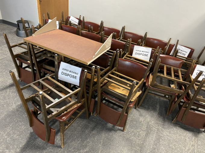 wood and reddish brown vinyl study chairs in a neatly stacked pile on a gray carpeted surface. 