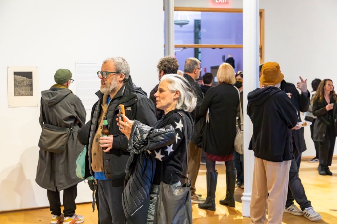 A handful of people stand in a gallery with wood floors, white walls. 