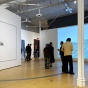 A handful of people stand in a gallery with wood floors, white walls, and a water-like artwork projection on far wall. 
