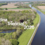 Zoom image: birds eye view of forests and farmlands bordering a canal, with "Medina Triennial 2026" overlaid in white text