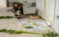 Jimena Murabito crouched and barefoot on a cement floor, working on a site-specific performance for Professor Millie Chen’s course, Installation: Urban Space, within a grain silo at "Silo City" in Buffalo, with cloth and ears of corn arranged on the ground in front of her. 
