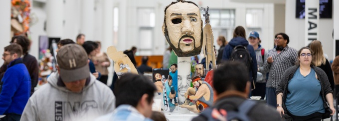 Zoom image: Guests amongst the displayed work: &quot;The Daltonverse&quot;, 2023, paper mache, oil paint, acrylic boards, cardboard, and paper, by MFA Candidate Dalton Carlson (MFA '24). Photo credit: Doug Levere. 
