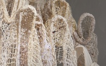 Sculptures made out of crocheted rope, that look like life-sized hooded figures, with a gray background, and white text. 