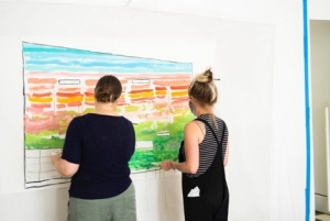 Zoom image: 2021 MFA graduate Sara Zak working with another volunteer on a painting at The Space Between. 