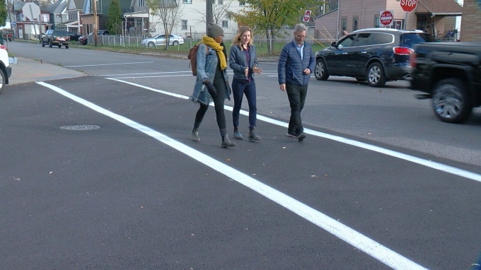 Three people walking down the street in freshly painted crosswalks. 