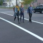 Three people walking down the street in freshly painted crosswalks. 