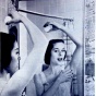 Woman with arm raised looking into a mirror, examining her underarm. 