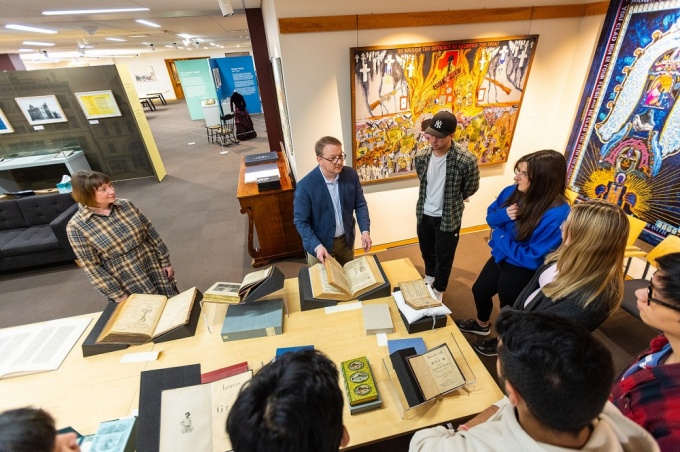 Art lecturer Kelly Myers-Chunco (far left) looks on while James Maynard (second from left), curator of the Poetry Collection and coordinator of the Rare & Special Books Collection, highlights one of the books he selected for students in Myers-Chunco’s typography class to examine. Photo: Douglas Levere. 
