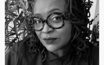Black and white headshot of artist Deborah Jack, wearing a button up shirt and large round, tortoise-patterned glasses. 