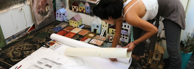 photograph of artist bent over drawing of houses. 