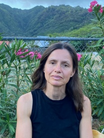 Zoom image: Yola Monakhov Stockton headshot wearing a black tank top in front of a chain link fence with flowers and mountains behind.