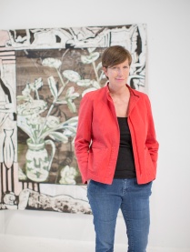 Zoom image: Joey Fauerso wearing a red blazer and blue jeans in front of a still life work of art depicting flowers in a vase, sketch style.