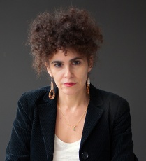 Zoom image: Karina Aguilera Skvirsky headshot, wearing a white shirt, black blazer, and dangling earrings.