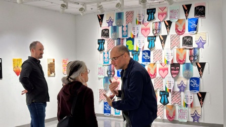 Zoom image: A group of people talking in front of a wall of felt penant flag artworks.