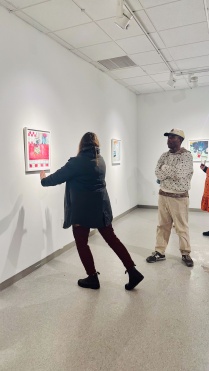 Zoom image: Joel Mulindwa speaking with visitors in Project Space gallery, for exhibition "Impressions of Gratuity", featuring his oil pastel drawings of tip jars.